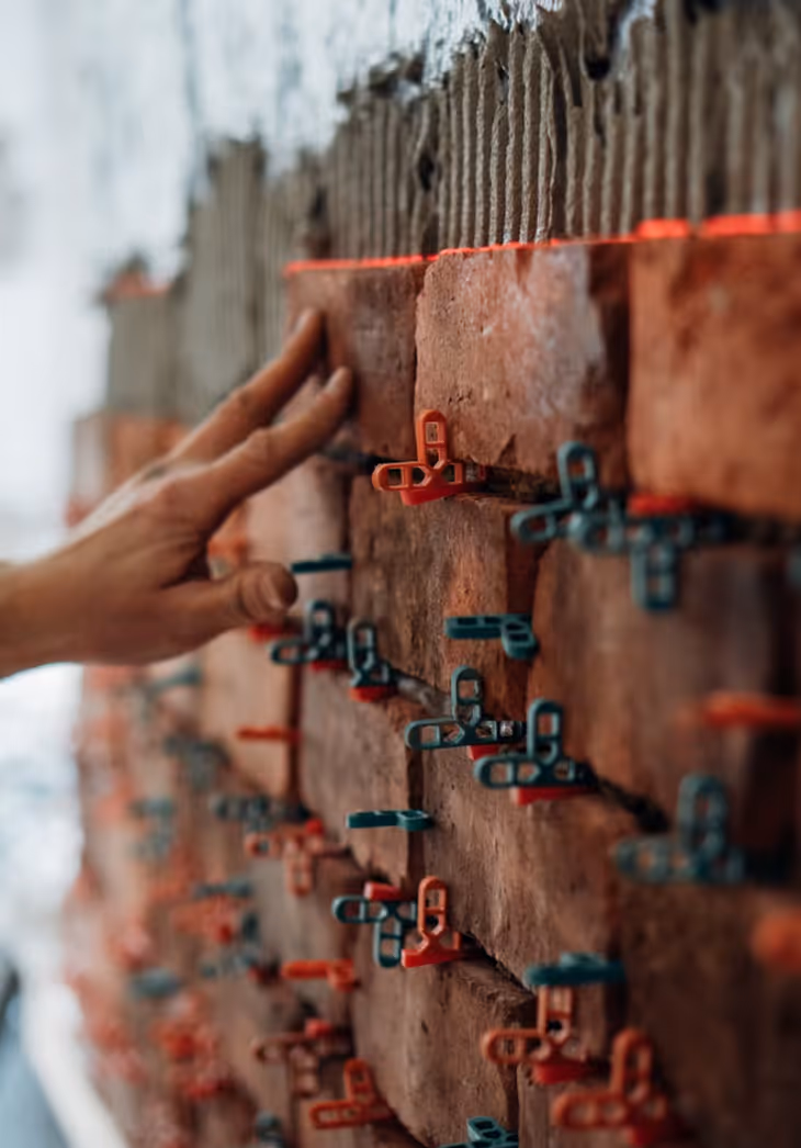 Professioneller Maurer beim Mauern einer Backsteinwand auf Baustelle in der Schweiz mit Maurerkelle und Wasserwaage